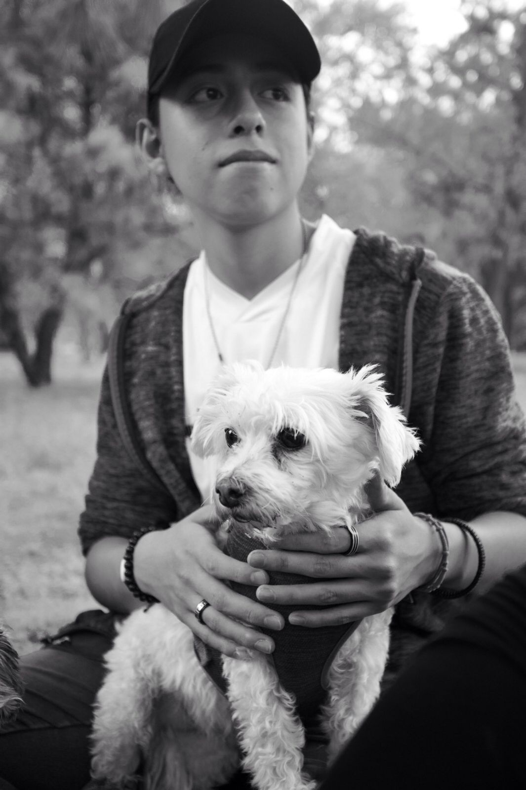 Joven en un parque sosteniendo un perro blanco pequeño, blanco y negro