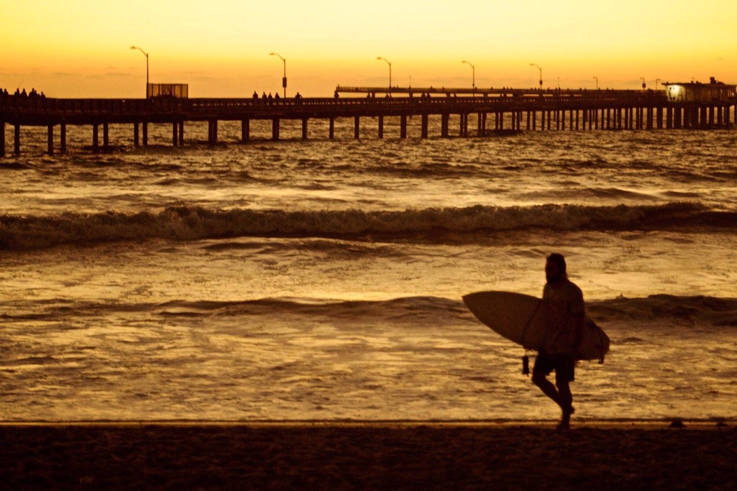 Surfista frente al muelle al atardecer